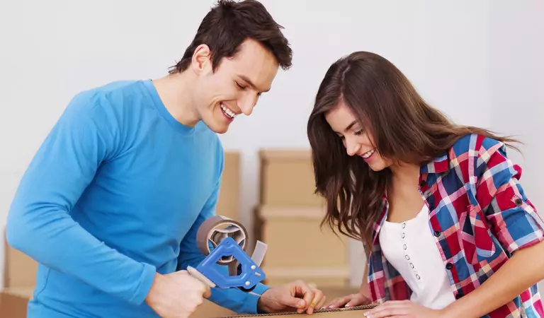 couple packing up cardboard box with a tape gun