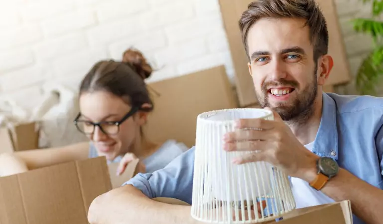 Young man unpacking a lamp from a box and a woman in the back