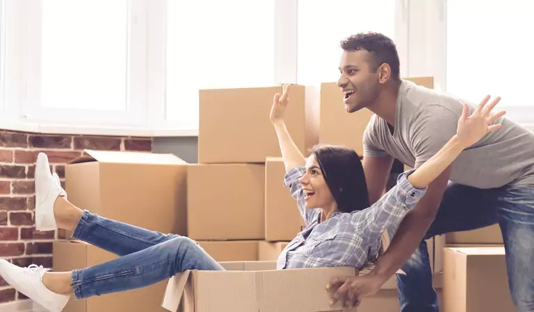woman sitting inside of a cardboard box and a young man pushing it from the back