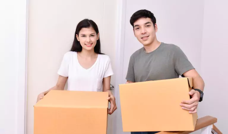 young couple holding cardboard boxes looking happy