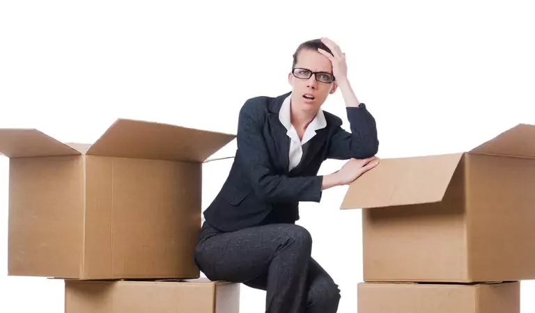 woman wearing specs looking stressed and sitting at the middle of cardboard boxes