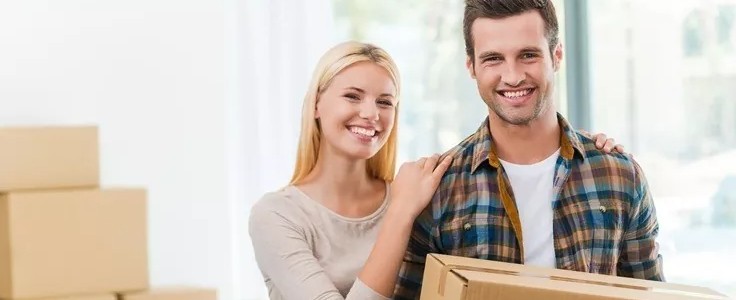 couple with a cardboard box looking happy inside of a new hosue