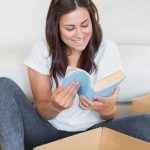 young woman reading a book and sitting in the middle of some cardboard boxes