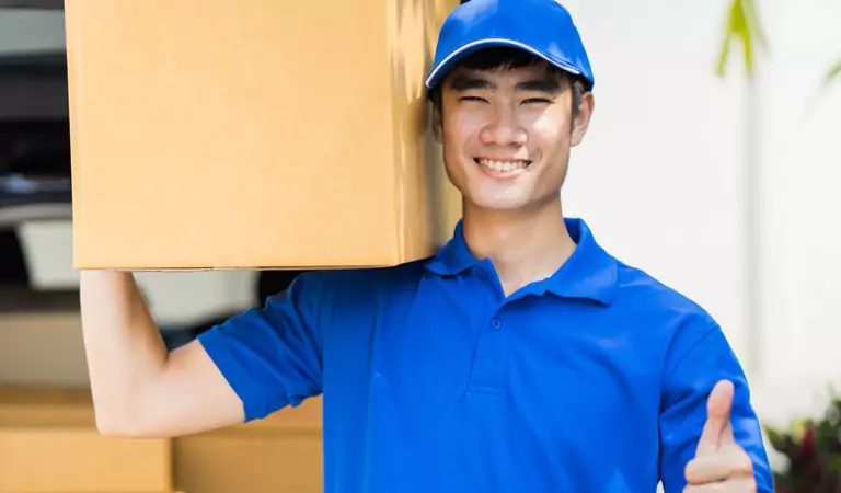 young man wearing blue cap and t-shirt holding a cardboard box on his shoulder