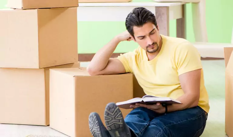 young man reading a book and sitting with some boxes